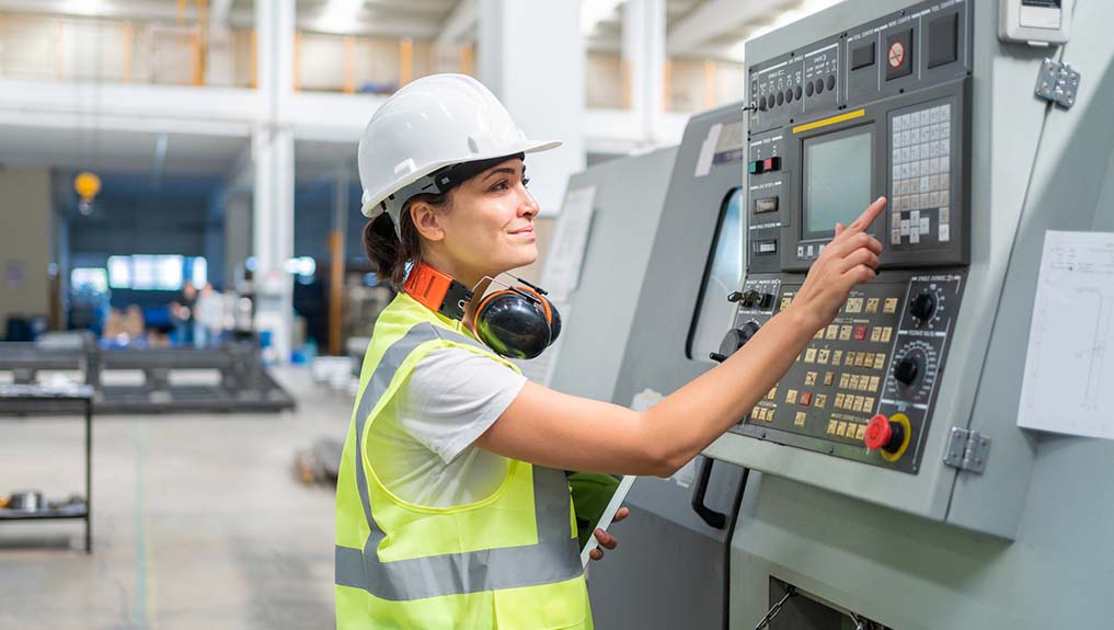 A female engineer wearing white safety helmet using a control panel on an industrial machine in a factory