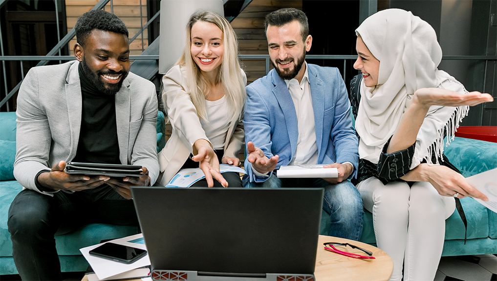 A group of four people smiling and looking at the screen
